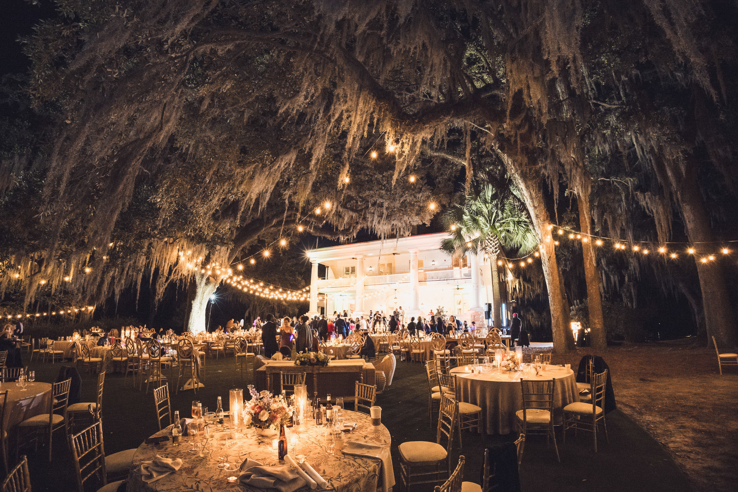 Outdoor wedding reception under oak trees with Spanish moss and string lights in front of Admiral’s House at night