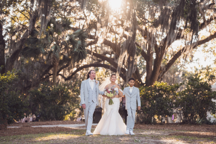 Bride walking with family beneath Spanish moss-covered live oaks on the way to her outdoor wedding ceremony.